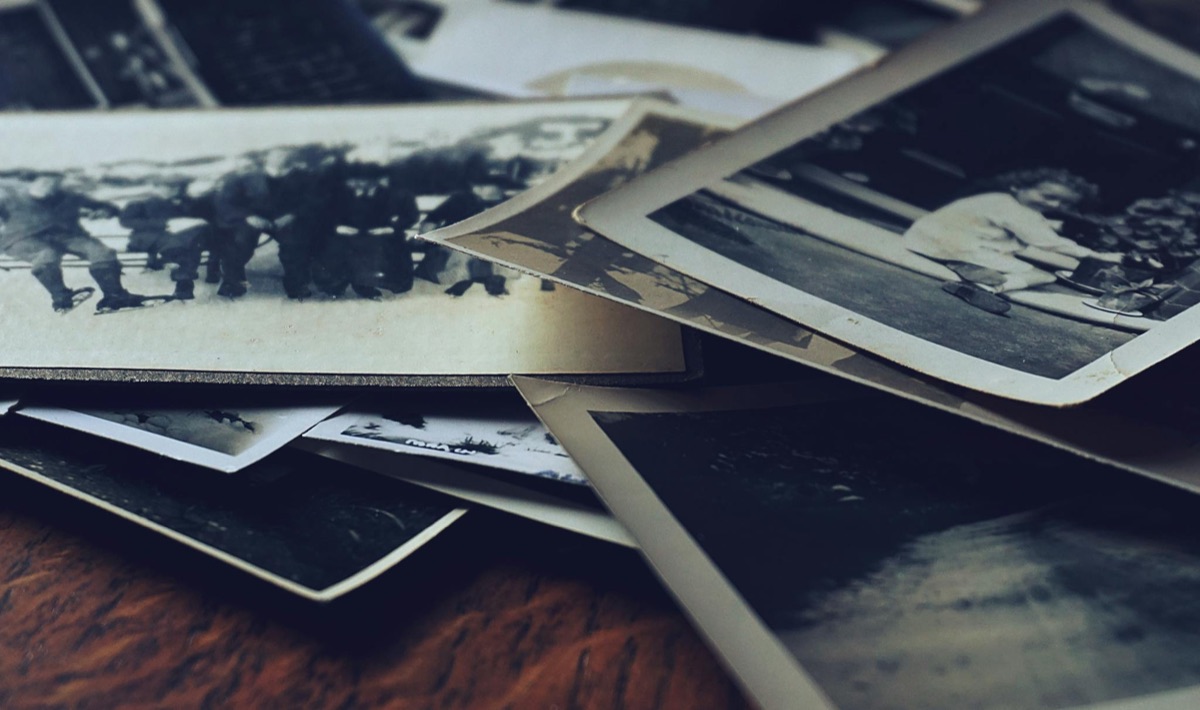 A scattered stack of classic black-and-white photographs on a wooden table